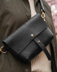 Black leather bag with gold accents on a person wearing a coat and sweater.