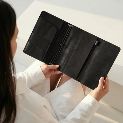 Person holding a black leather wallet against a neutral background