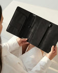 Person holding a black leather wallet against a neutral background