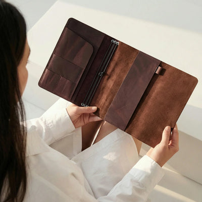 Person holding a brown leather portfolio against a neutral background