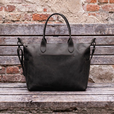 Black leather bag on a wooden surface with a brick wall background