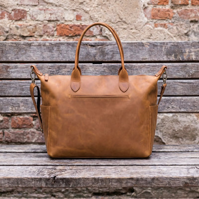 Brown leather bag on a wooden surface with a rustic brick wall background