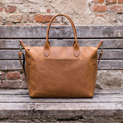 Brown leather bag on a wooden surface with a rustic brick wall background