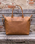 Brown leather bag on a wooden surface with a rustic brick wall background