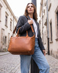 Woman holding a brown leather bag on a cobblestone street.