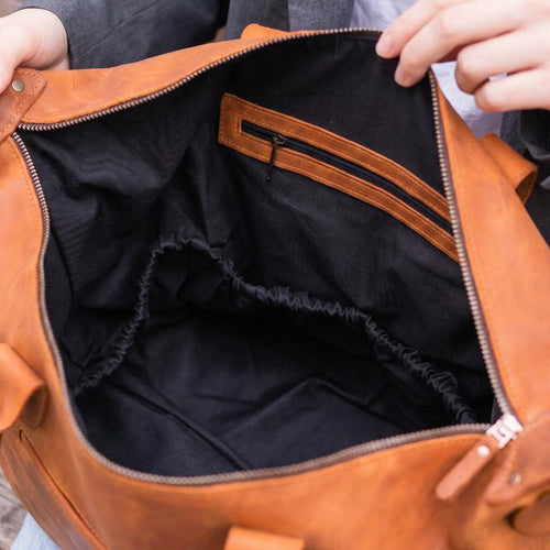 Brown leather bag with black interior being held open by a person.