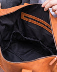 Brown leather bag with black interior being held open by a person.