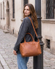 Woman holding a brown leather handbag on a city street.