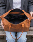 Person holding a brown leather bag with wooden bench background