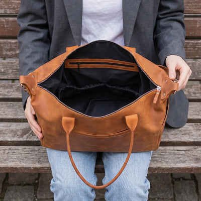 Person holding a brown leather bag with wooden bench background