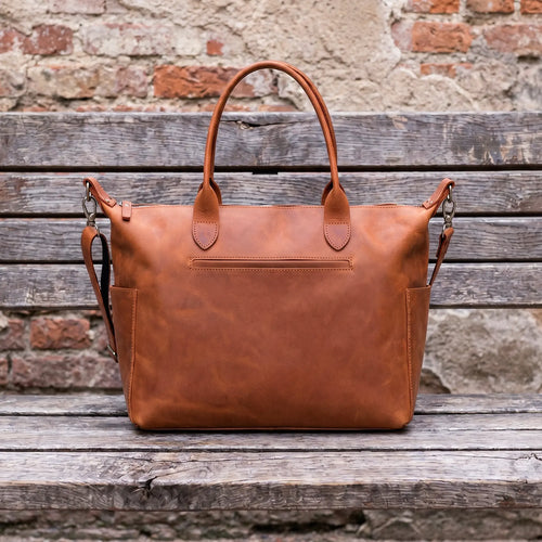 Brown leather bag on a wooden surface with a rustic brick wall background