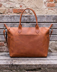 Brown leather bag on a wooden surface with a rustic brick wall background