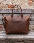 Brown leather bag on a wooden surface with a rustic brick wall background