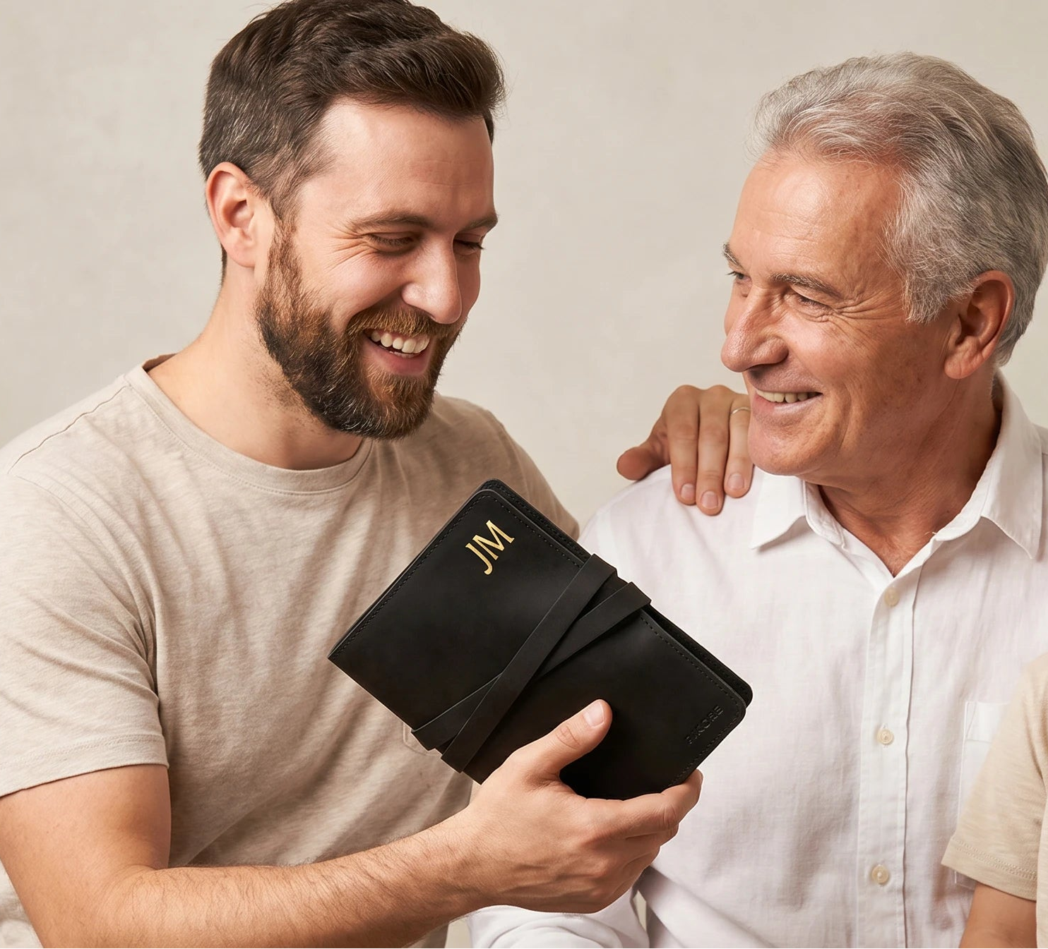 Three generations of men, including a father, son, and grandfather, holding a black leather-bound book against a plain background.