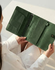 Person holding a green leather wallet against a neutral background