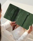 Person holding a green wallet with a neutral background