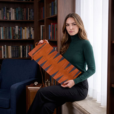 Woman holding a brown leather suitcase in a room with bookshelves and a blue chair.