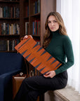 Woman holding a brown leather suitcase in a room with bookshelves and a blue chair.