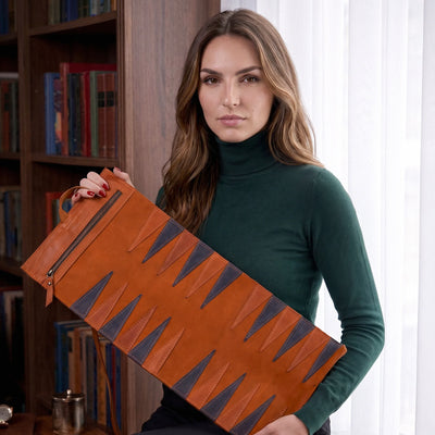 Woman holding a brown leather bag with geometric patterns in a room with bookshelves.