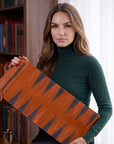 Woman holding a brown leather bag with geometric patterns in a room with bookshelves.