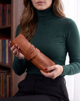 Person holding a brown leather roll with a bookshelf in the background