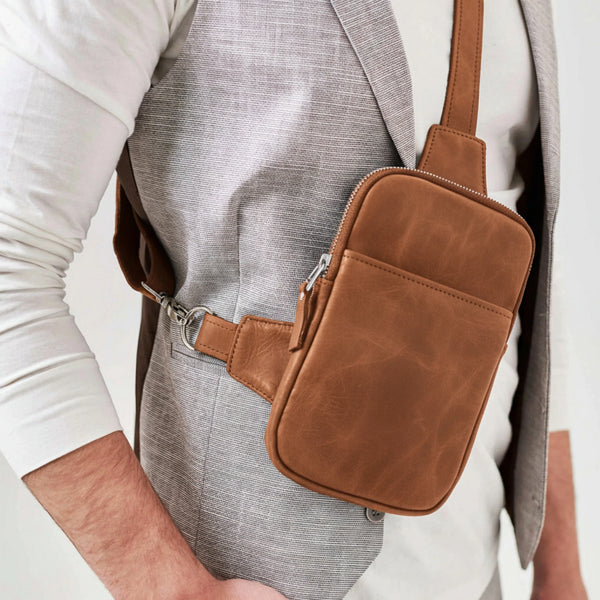 Brown leather crossbody bag worn by a person on a plain background