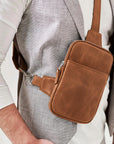 Brown leather crossbody bag worn by a person on a plain background
