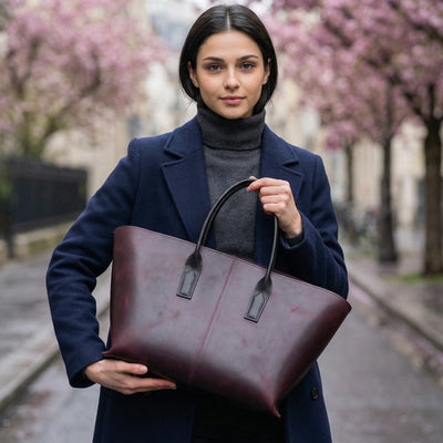 Woman holding a brown leather tote bag in an urban setting with cherry blossoms.