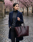 Woman in a blue coat holding a maroon bag on a cobbled street with cherry blossom trees in the background.
