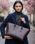 Woman holding a brown leather tote bag in an urban setting with cherry blossoms.