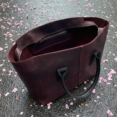 Brown leather tote bag on a surface with scattered pink petals