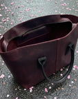 Brown leather tote bag on a surface with scattered pink petals