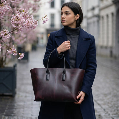 Woman holding a brown leather tote bag on a city street with cherry blossoms.