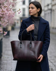 Woman holding a brown leather tote bag on a city street with cherry blossoms.