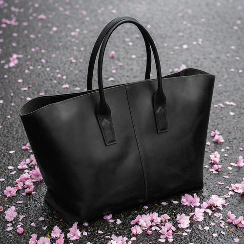 Black tote bag on a gray surface with pink flower petals
