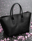 Black tote bag on a gray surface with pink flower petals