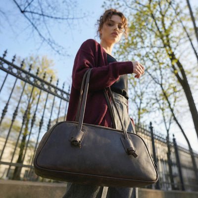 Woman holding a black handbag outdoors with trees and a fence in the background