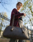 Woman holding a black handbag outdoors with trees and a fence in the background