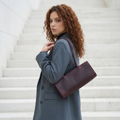Woman in a gray coat holding a burgundy handbag on a white staircase