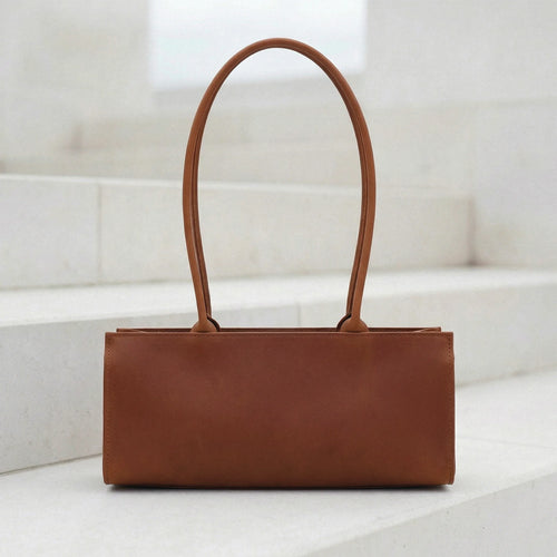 Brown leather handbag on a white surface with a light background