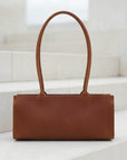 Brown leather handbag on a white surface with a light background