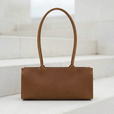 Brown leather handbag on a white surface with a light background