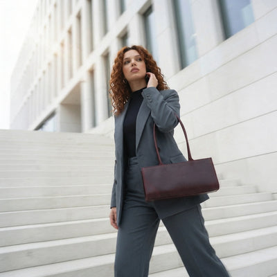 Woman in a gray suit with a brown handbag standing on steps in front of a modern building.