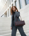 Woman in a gray suit with a brown handbag standing on steps in front of a modern building.