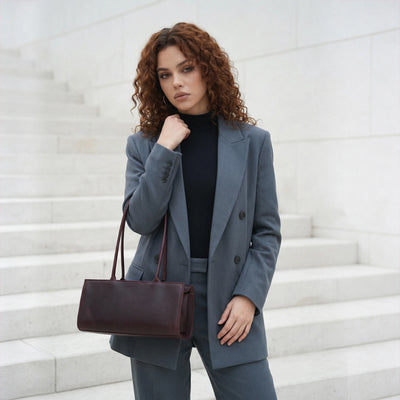 Woman in a gray suit holding a brown leather bag on a white background
