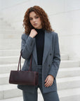 Woman in a gray suit holding a brown leather bag on a white background