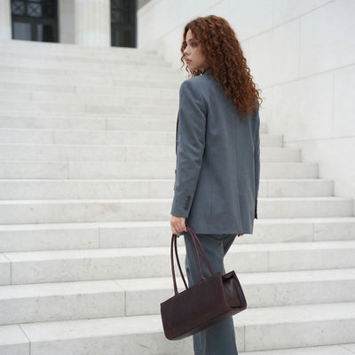 Woman in a gray suit holding a brown handbag on marble steps