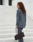 Woman in a gray suit holding a brown handbag on marble steps