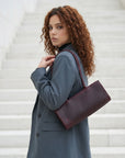 Woman in a gray coat holding a burgundy handbag on a white staircase