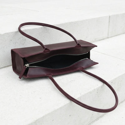 Brown leather handbag with a shoulder strap on a light gray background